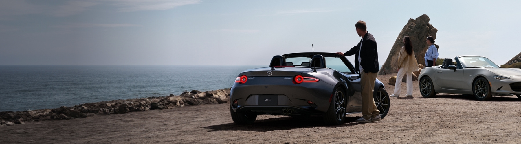 2026 Mazda MX-5 Miata parked on a coastal overlook, rear three-quarter view.