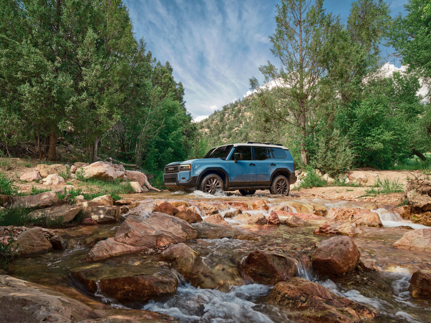 2026 Toyota Land Cruiser fording a rocky stream in a forest.