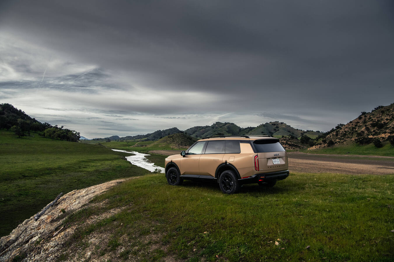 2027 Kia Telluride X-Pro fording a shallow river, tan exterior, official Kia press photography.