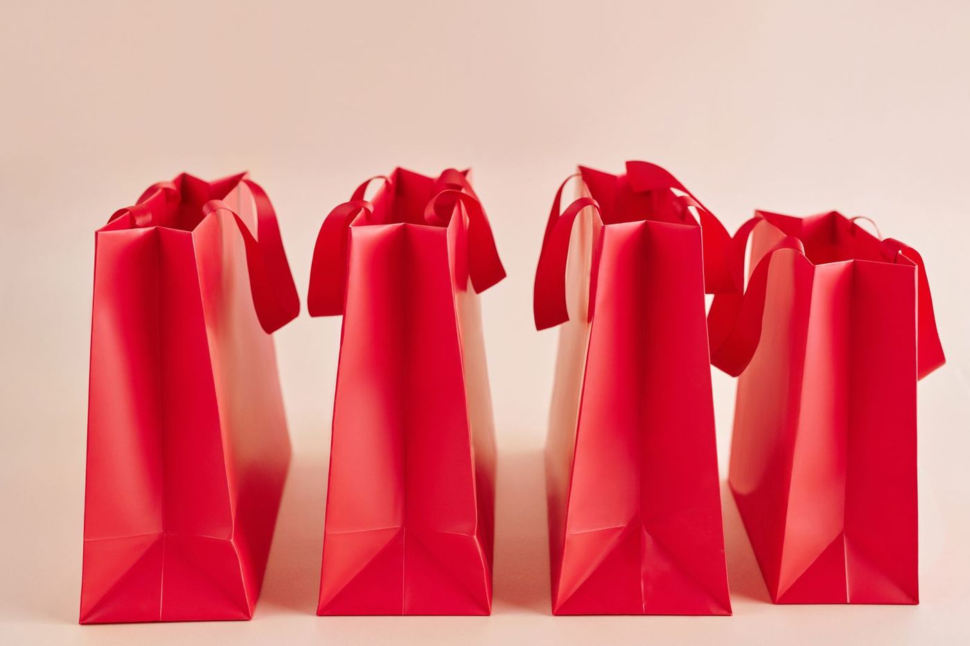 Row of red paper shopping bags against a pink background