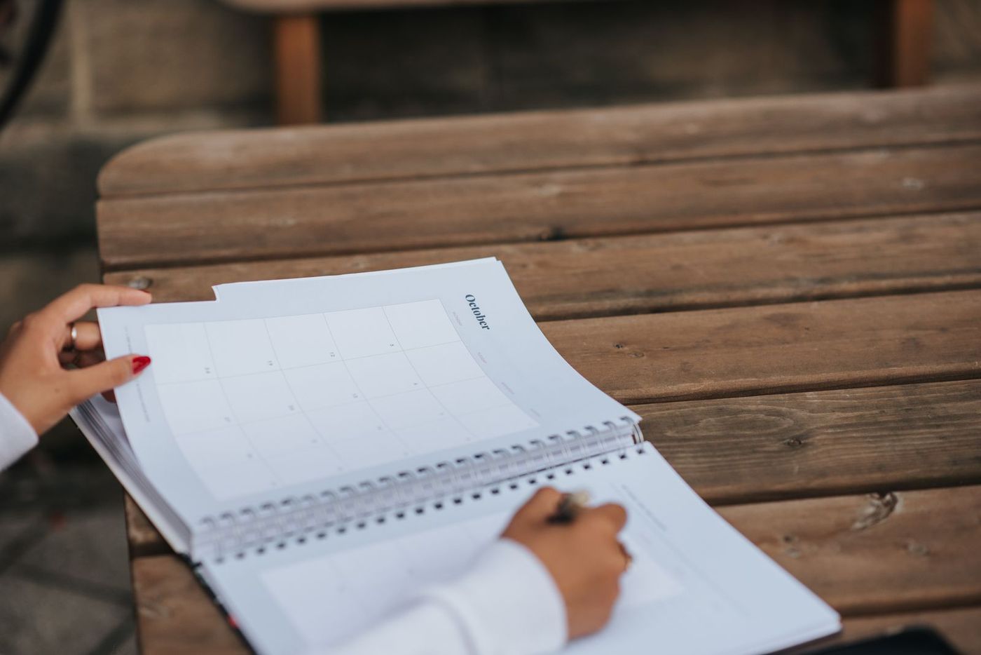 Planner notebook open on a wooden bench with a hand writing