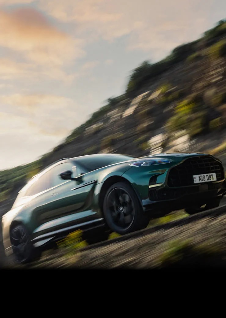 Aston Martin DBX707 cornering at speed on a coastal mountain road.