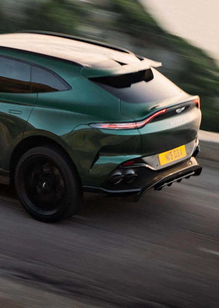 Rear three-quarter view of the Aston Martin DBX707 driving on a road.