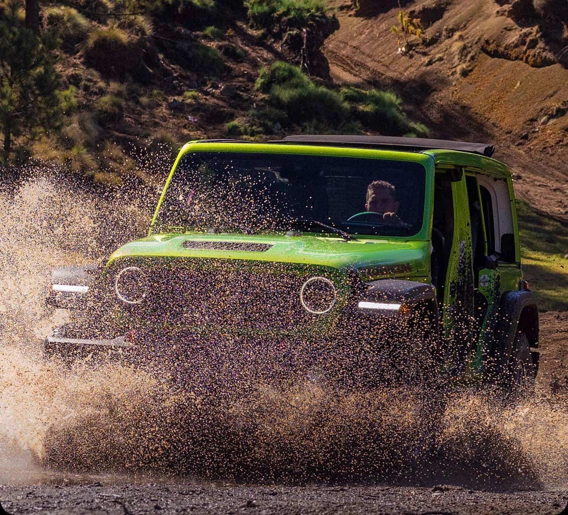 A Jeep Wrangler with 4WD driving through mud and water.