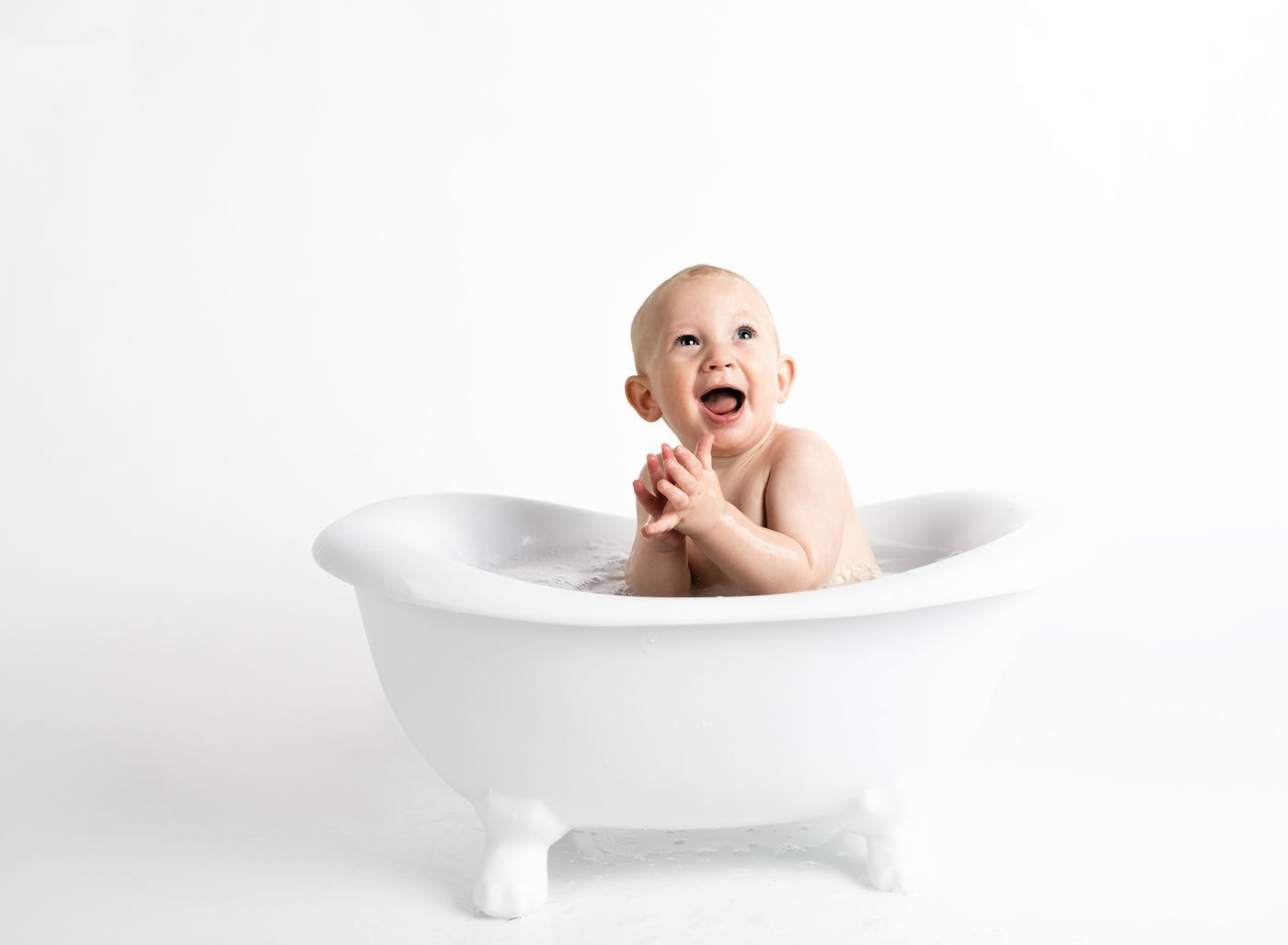 A laughing baby sitting in a small white tub against a white backdrop