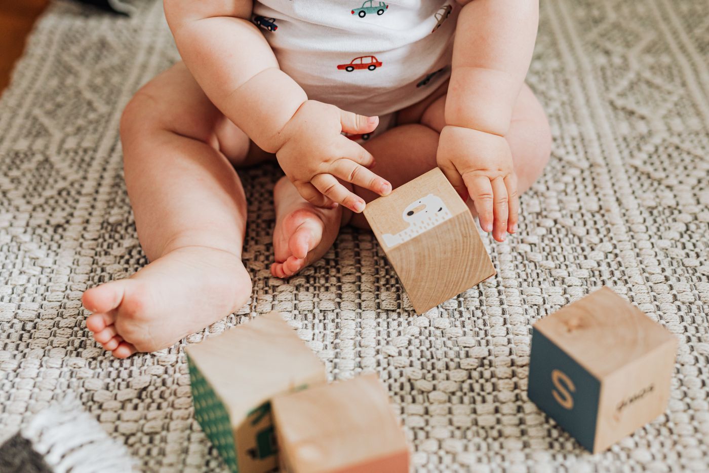 A baby sitting on a woven rug exploring wooden blocks