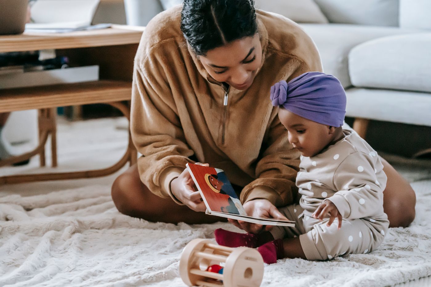 A parent and baby sitting on a rug looking at a picture book