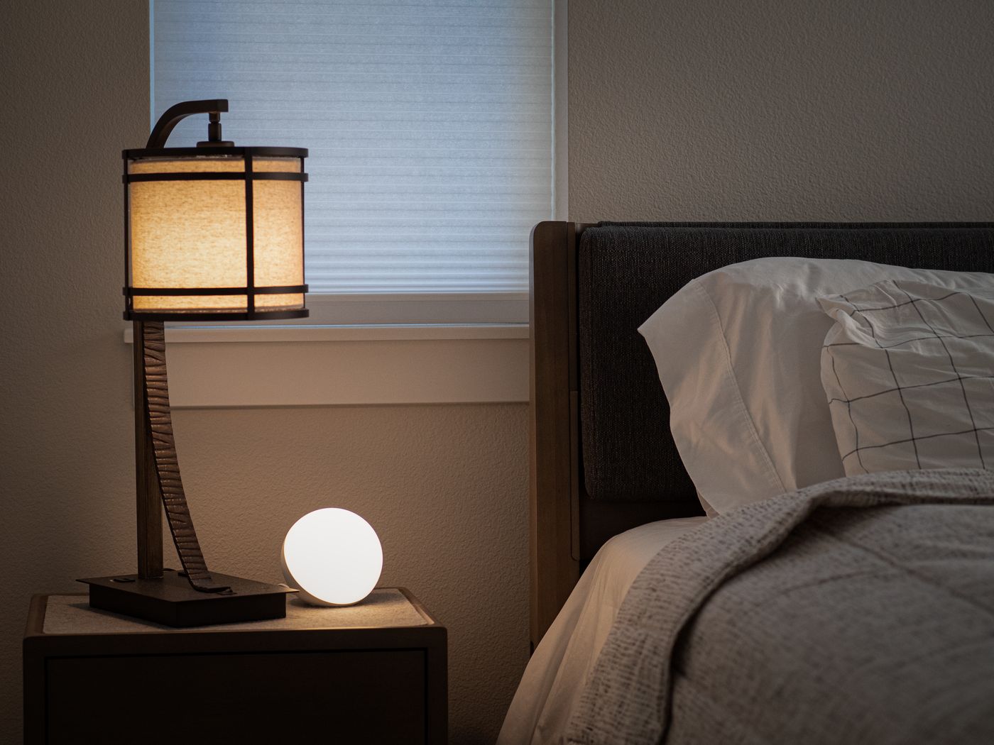 A small glowing round lamp beside a larger table lamp on a nightstand