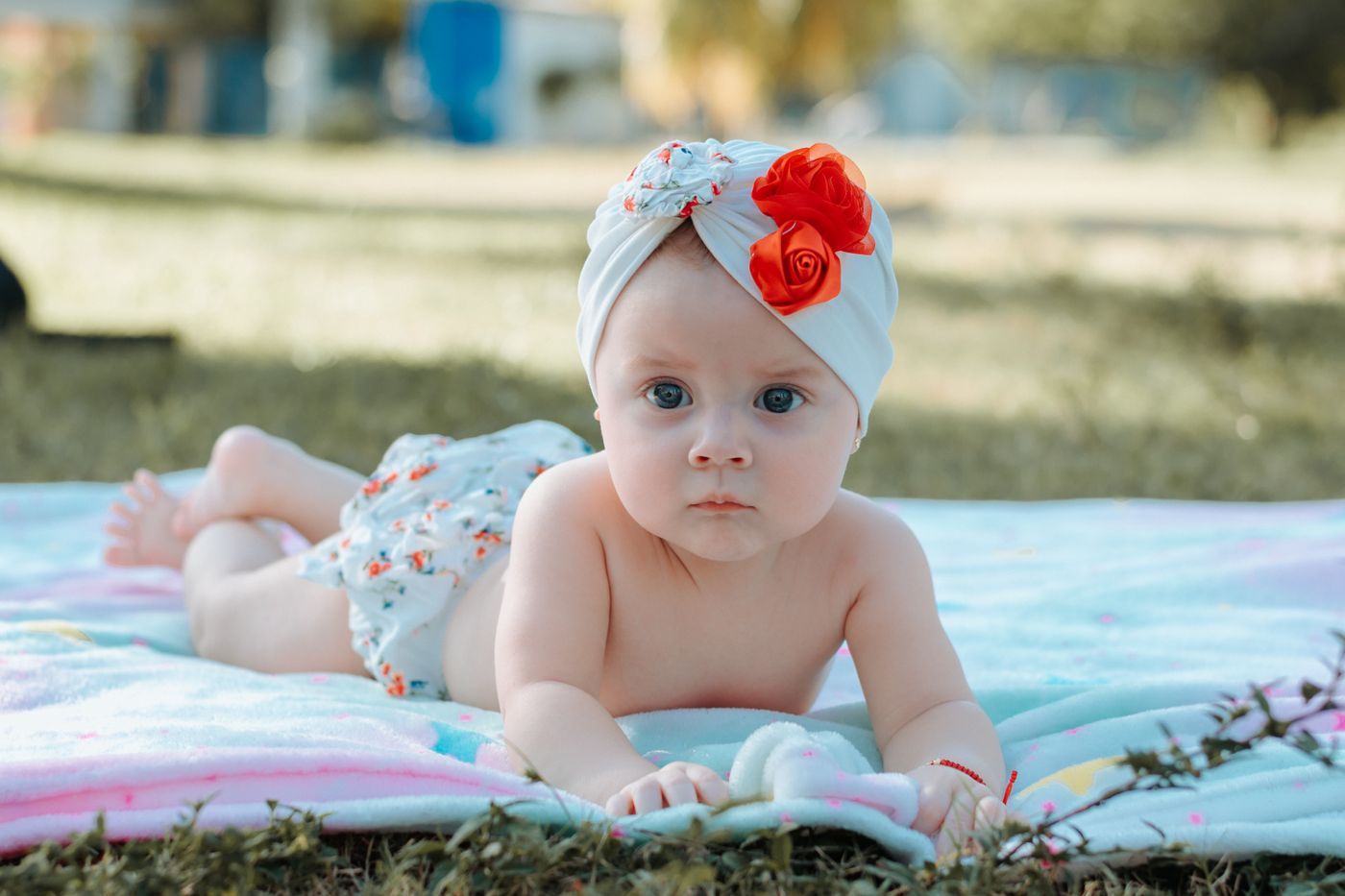 A baby lying on their tummy on a soft blanket outdoors, looking at the camera