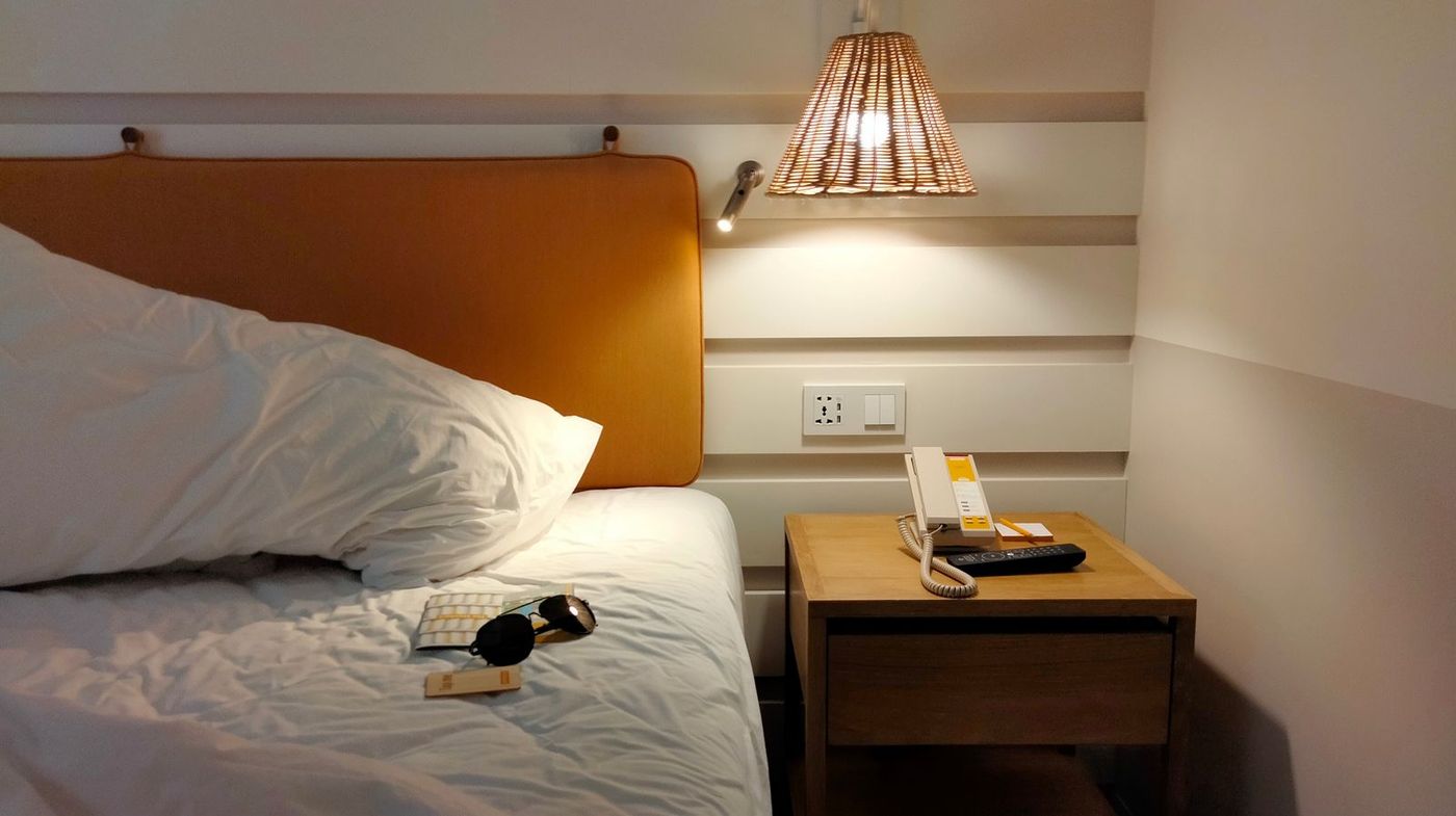 Bed with a pillow and a lit lamp on a bedside table