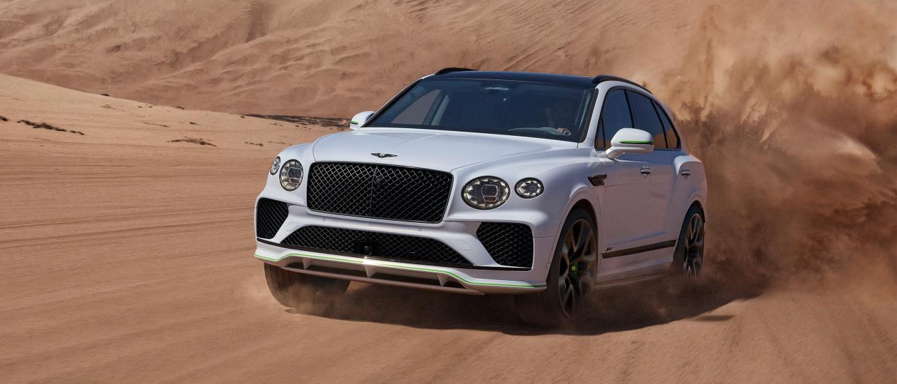 Bentley Bentayga in white, driving through desert sand dunes.