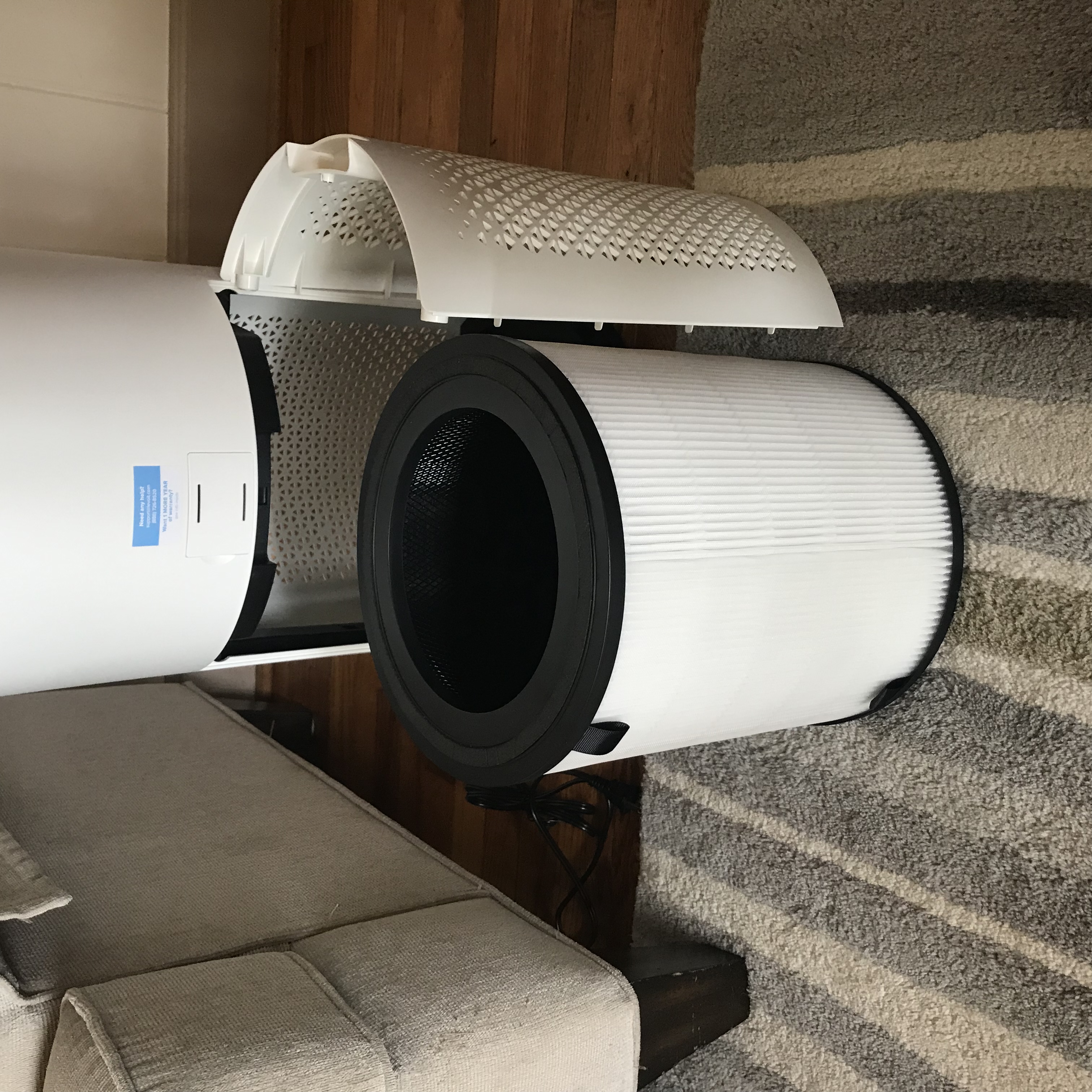 A tower-style HEPA air purifier running on a wood floor in a living room, real photograph.