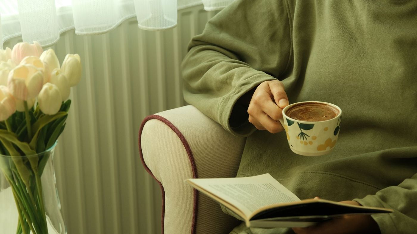 A woman reading in an armchair with a cup of coffee and a bouquet of tulips