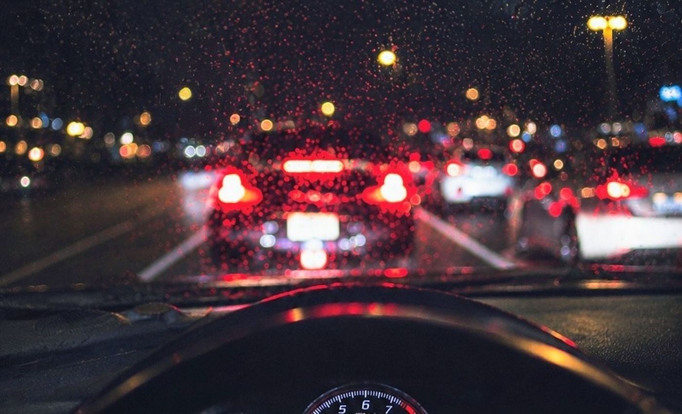 Dusk traffic seen through a rainy windshield, the scene a front camera is meant to record.