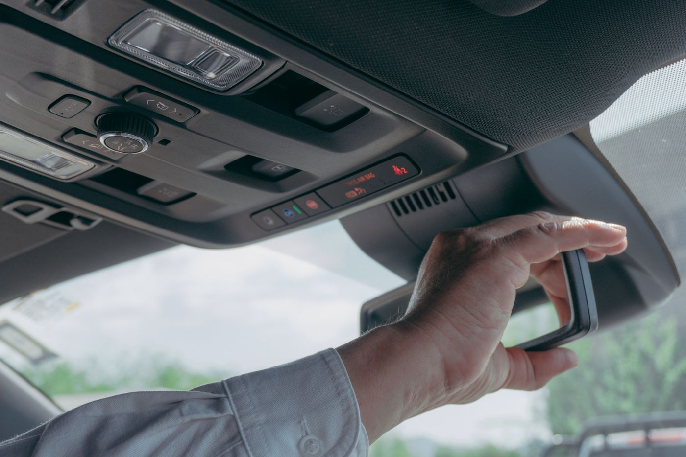 A driver reaching up to the rearview mirror area, where many dash cams mount.