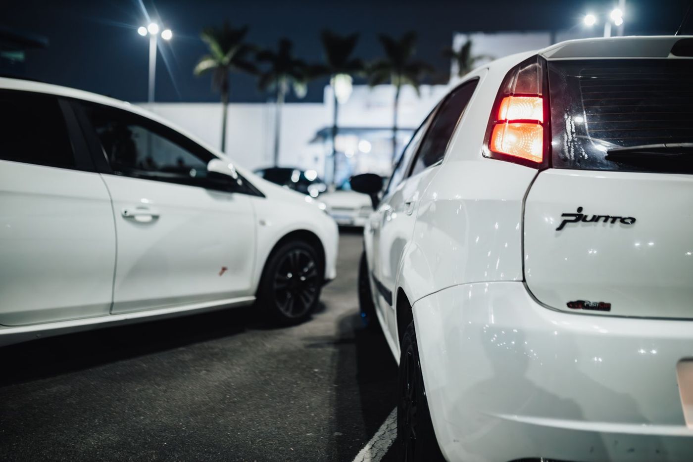 A white hatchback tail light in a night parking lot, a view a rear-facing camera is meant to capture.