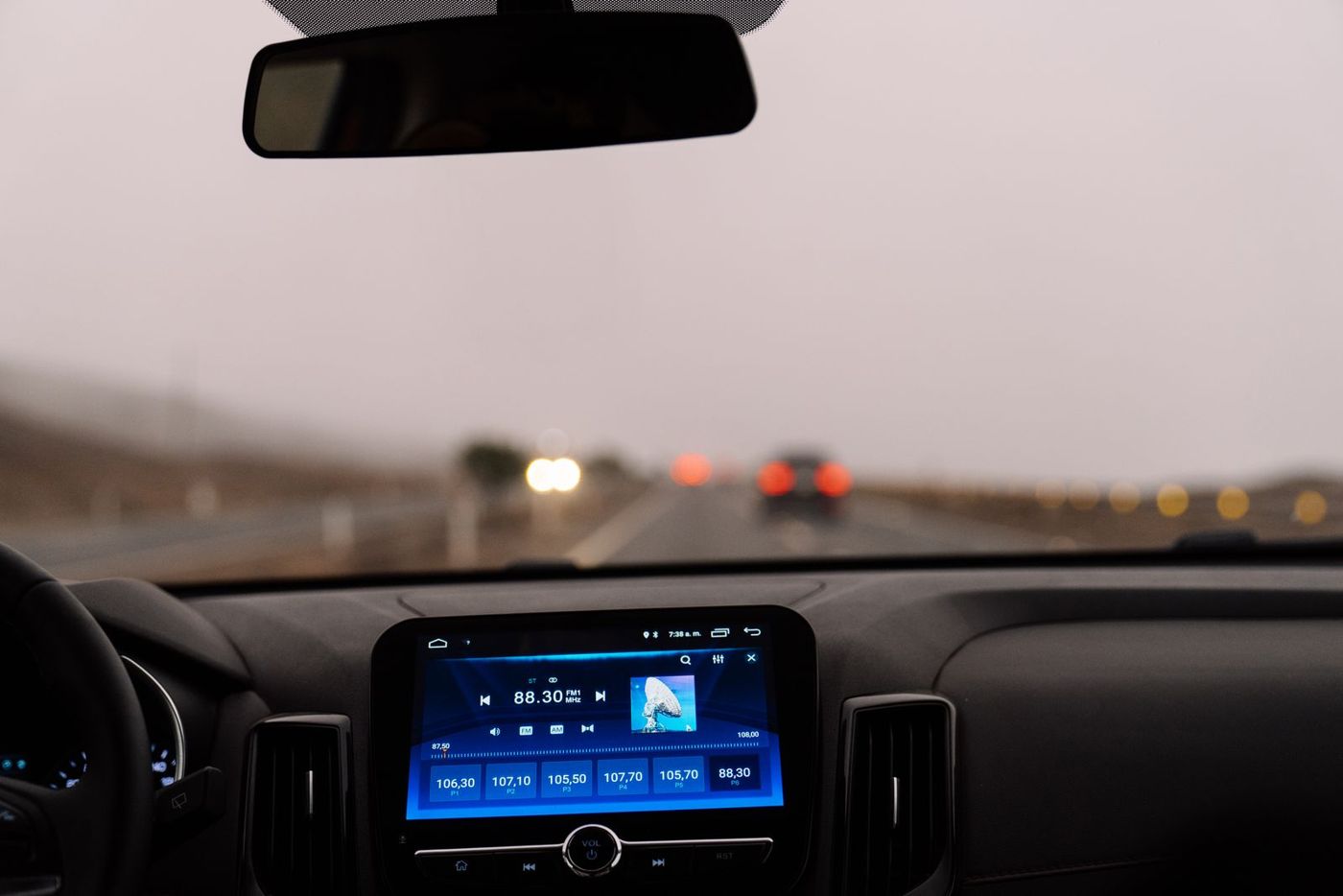 View through a car windshield of an open road, with the dashboard screen and rearview mirror in frame