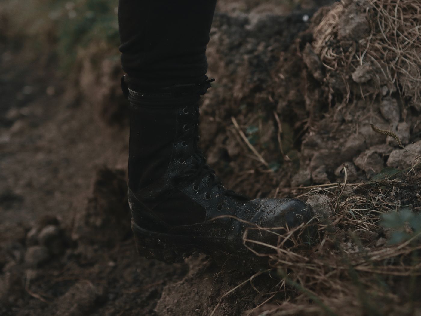 Black lug-sole lace-up boot stepping on dirt