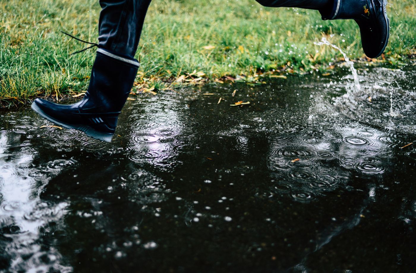 Person in dark rubber boots splashing through a puddle