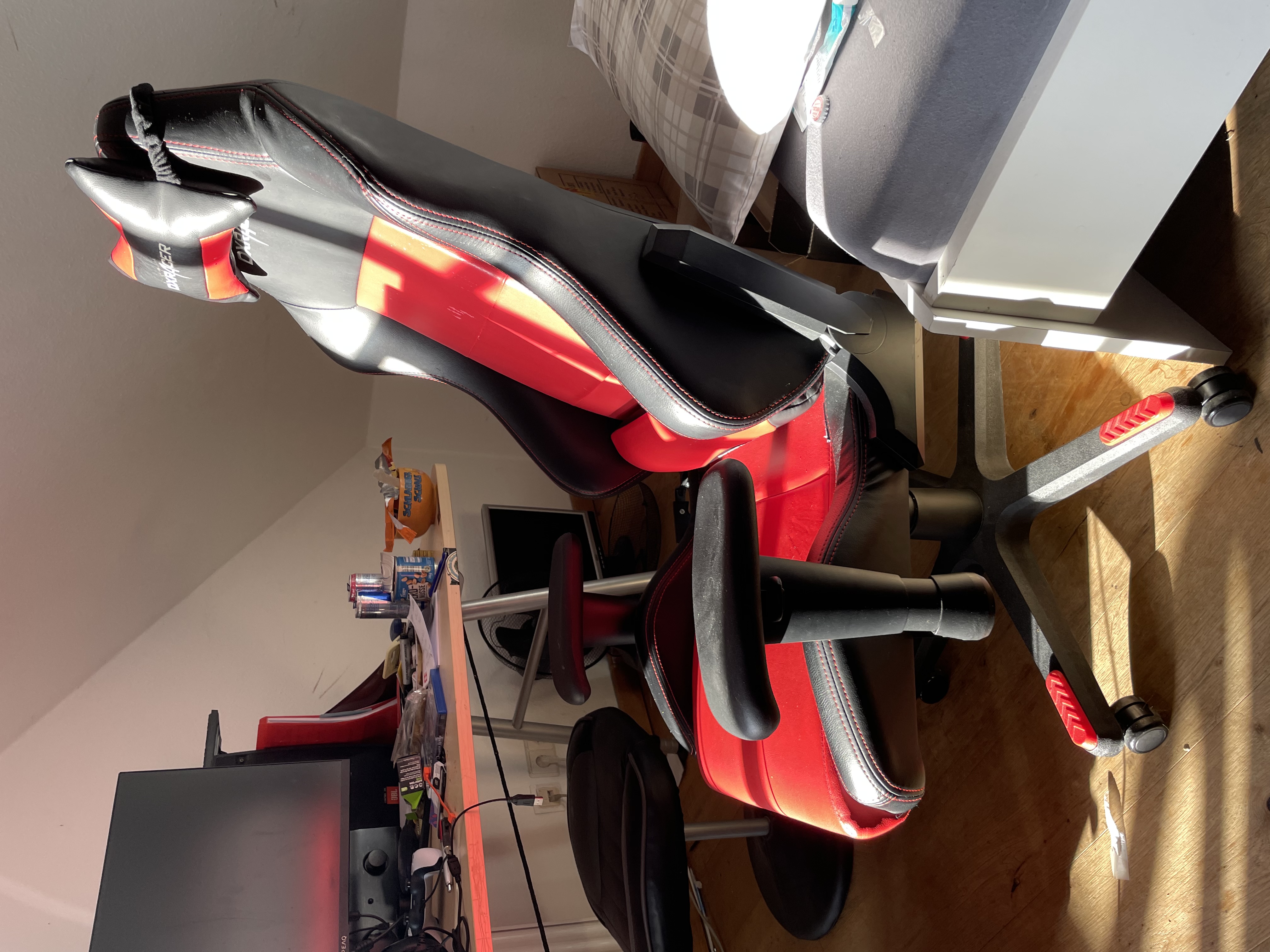 A racing-style gaming chair with adjustable armrests set up at a desk with a monitor, real photograph.