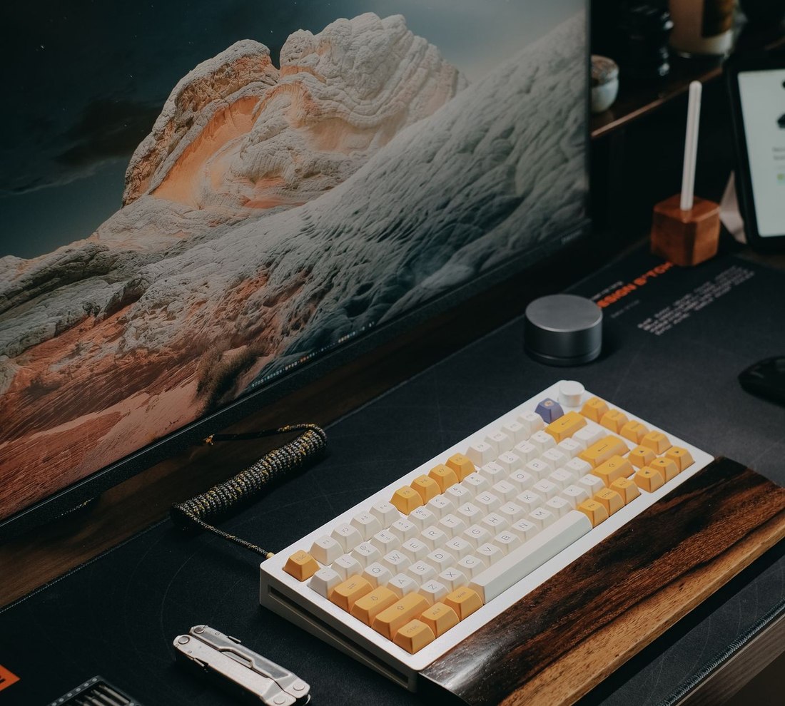 A tidy desk setup: monitor, compact mechanical keyboard on a desk mat, and cable-managed accessories