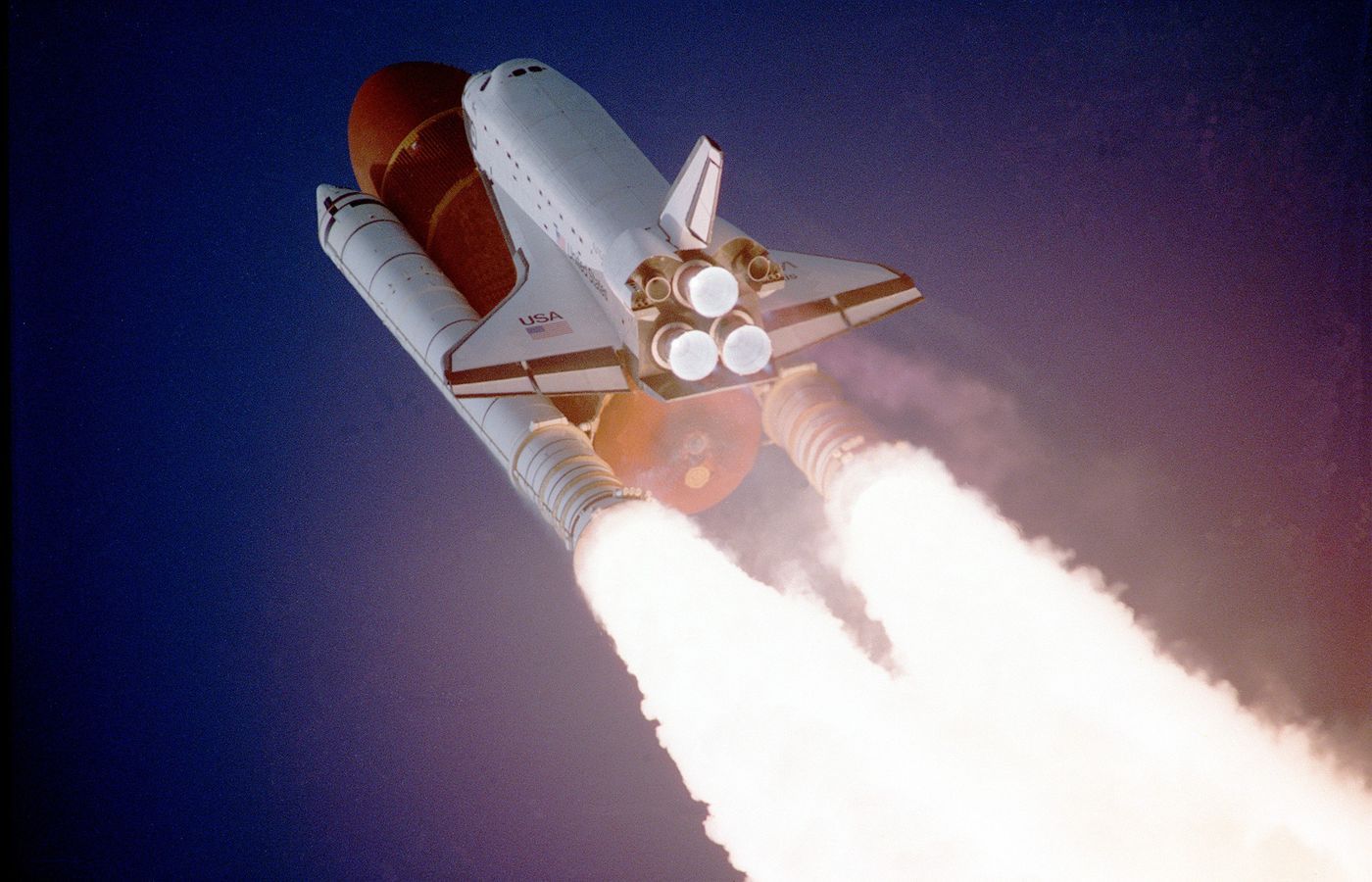 A white space shuttle lifting off into a deep blue sky with a bright exhaust plume