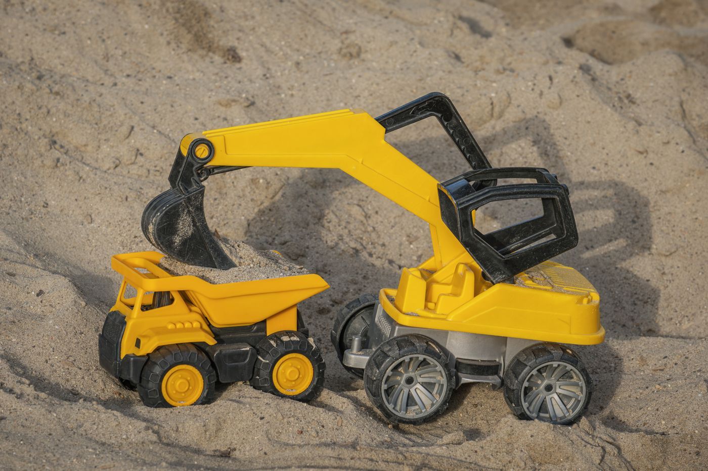 A yellow toy excavator and dump truck resting on sand