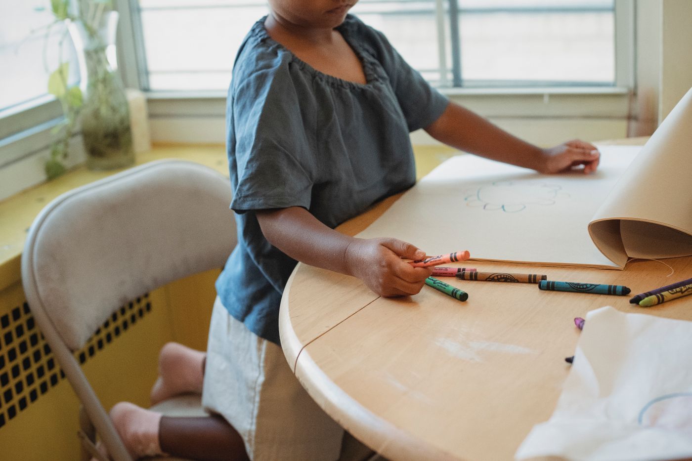 A child's hand drawing with crayons at a table