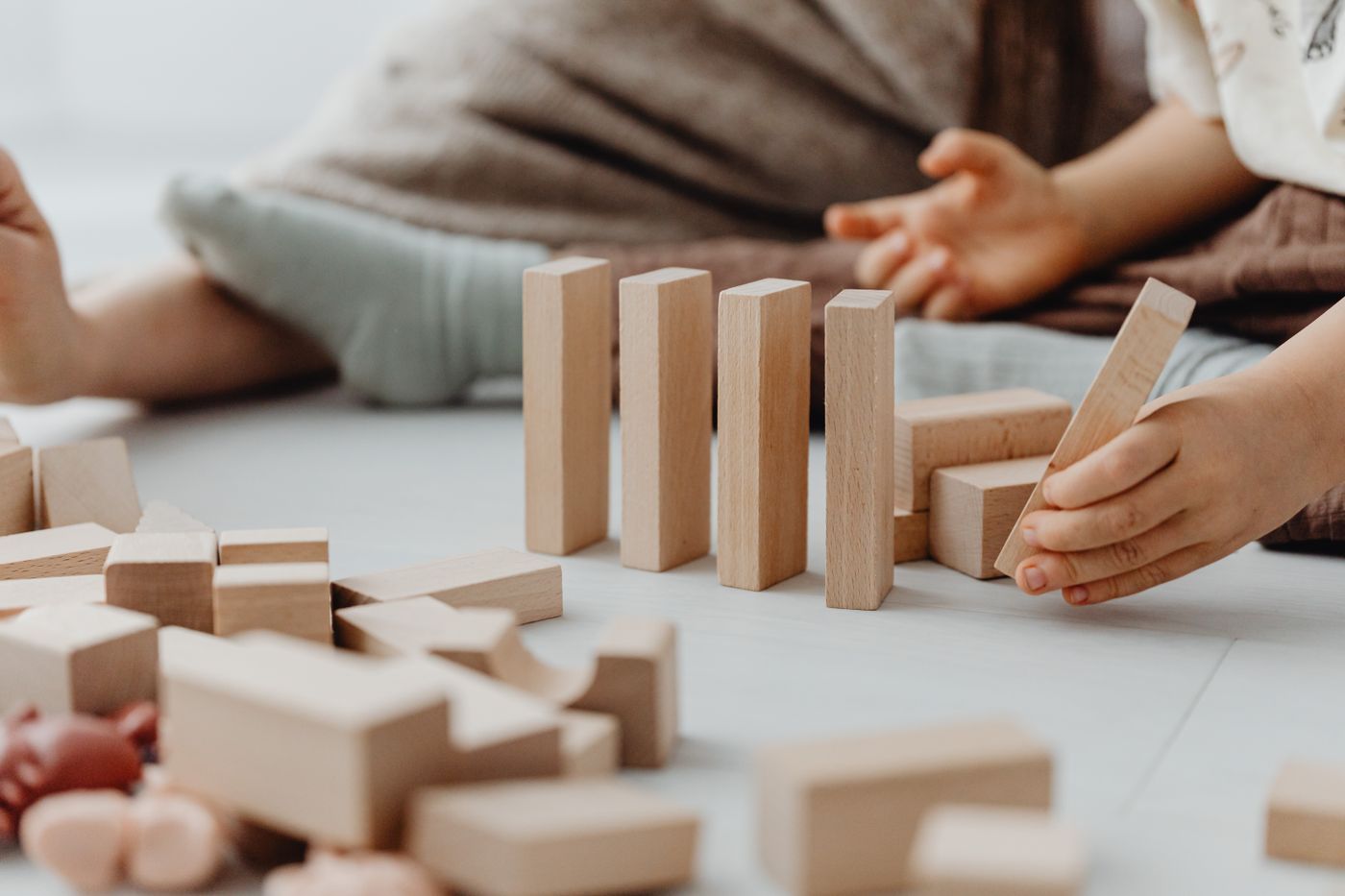A child's hands building with natural wooden blocks on a light floor