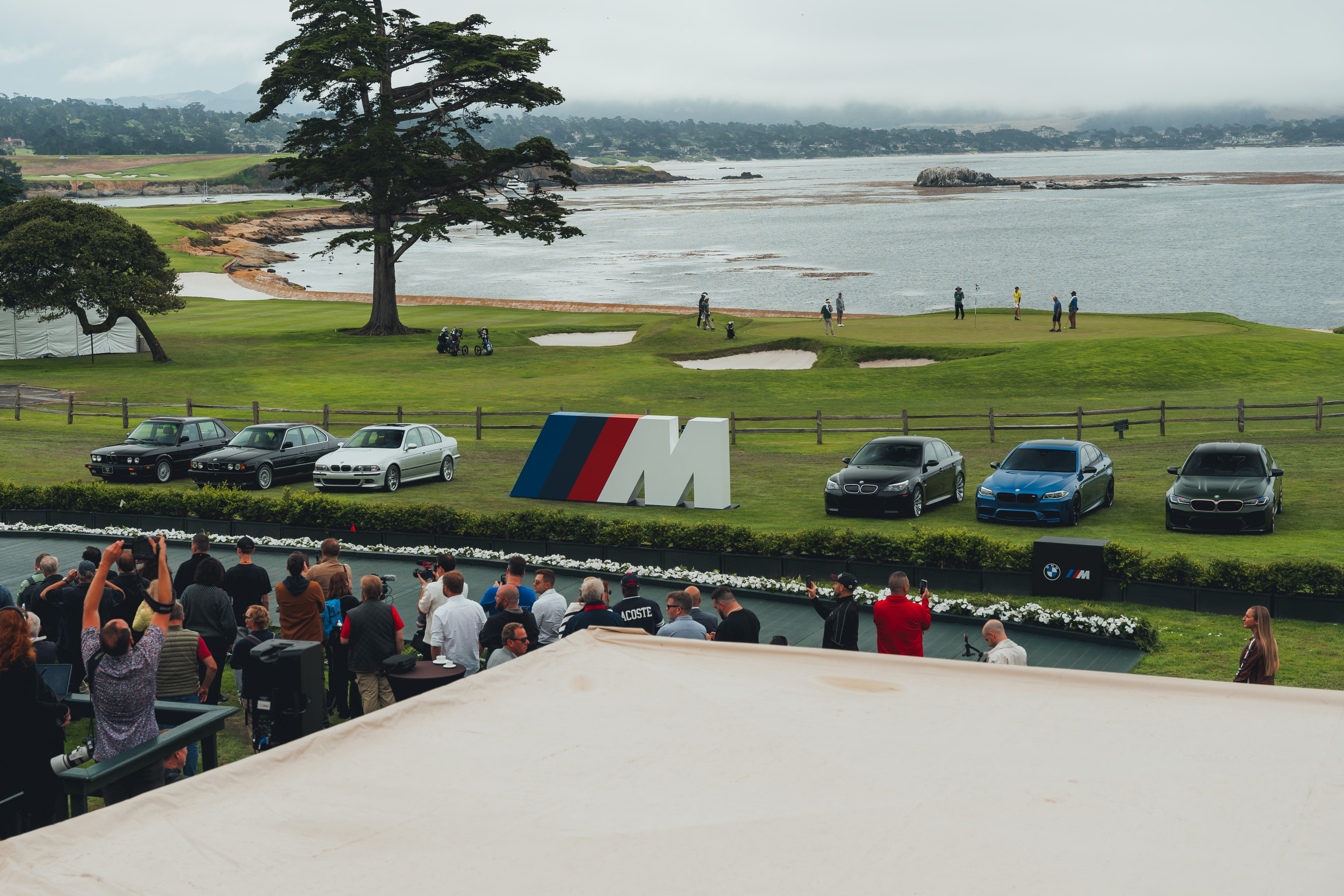 A lineup of current and historic BMW M5 generations on display at the model's world premiere event, overlooking the coast.