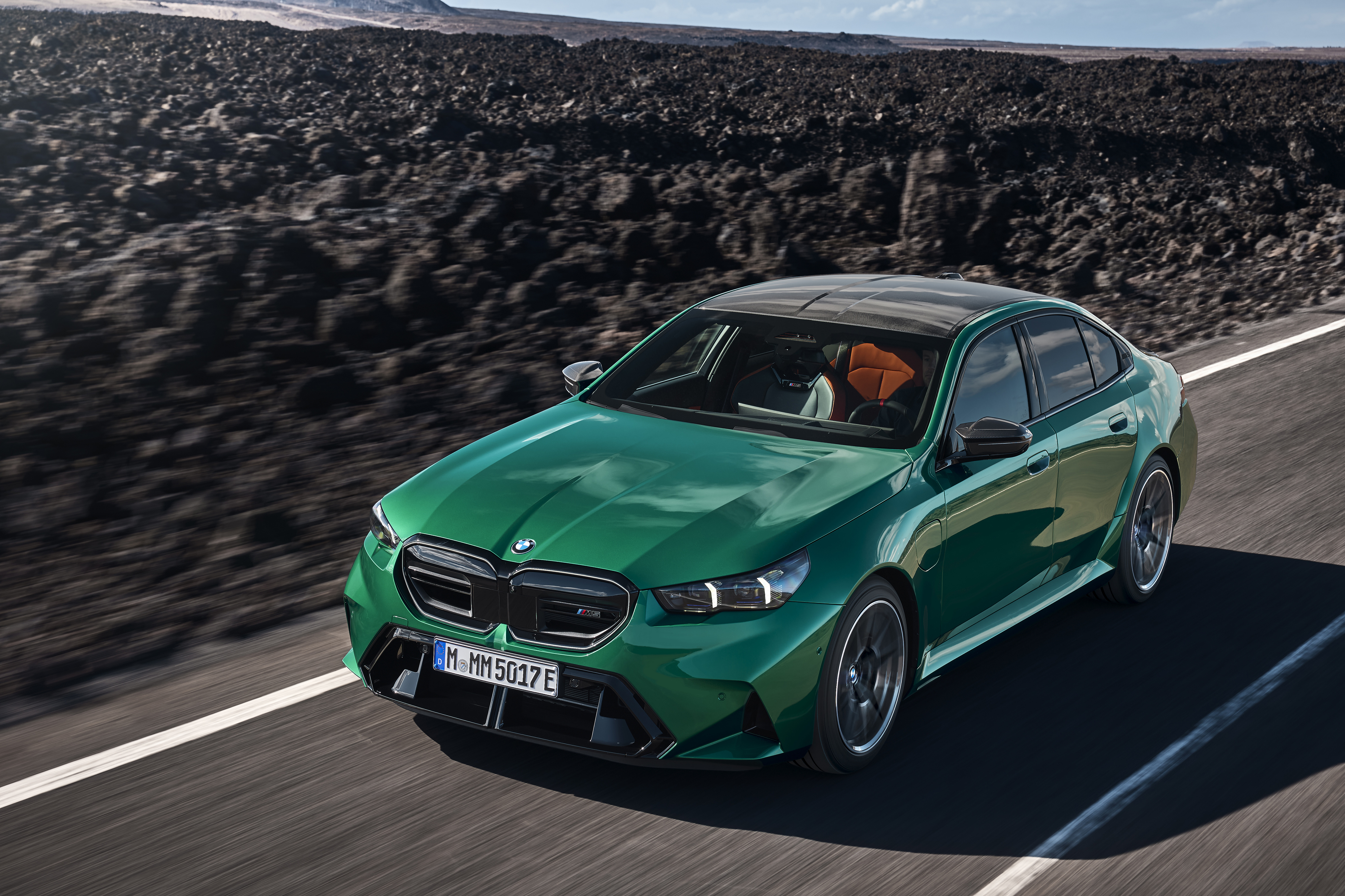 2027 BMW M5 in green, driving on a coastal mountain road.