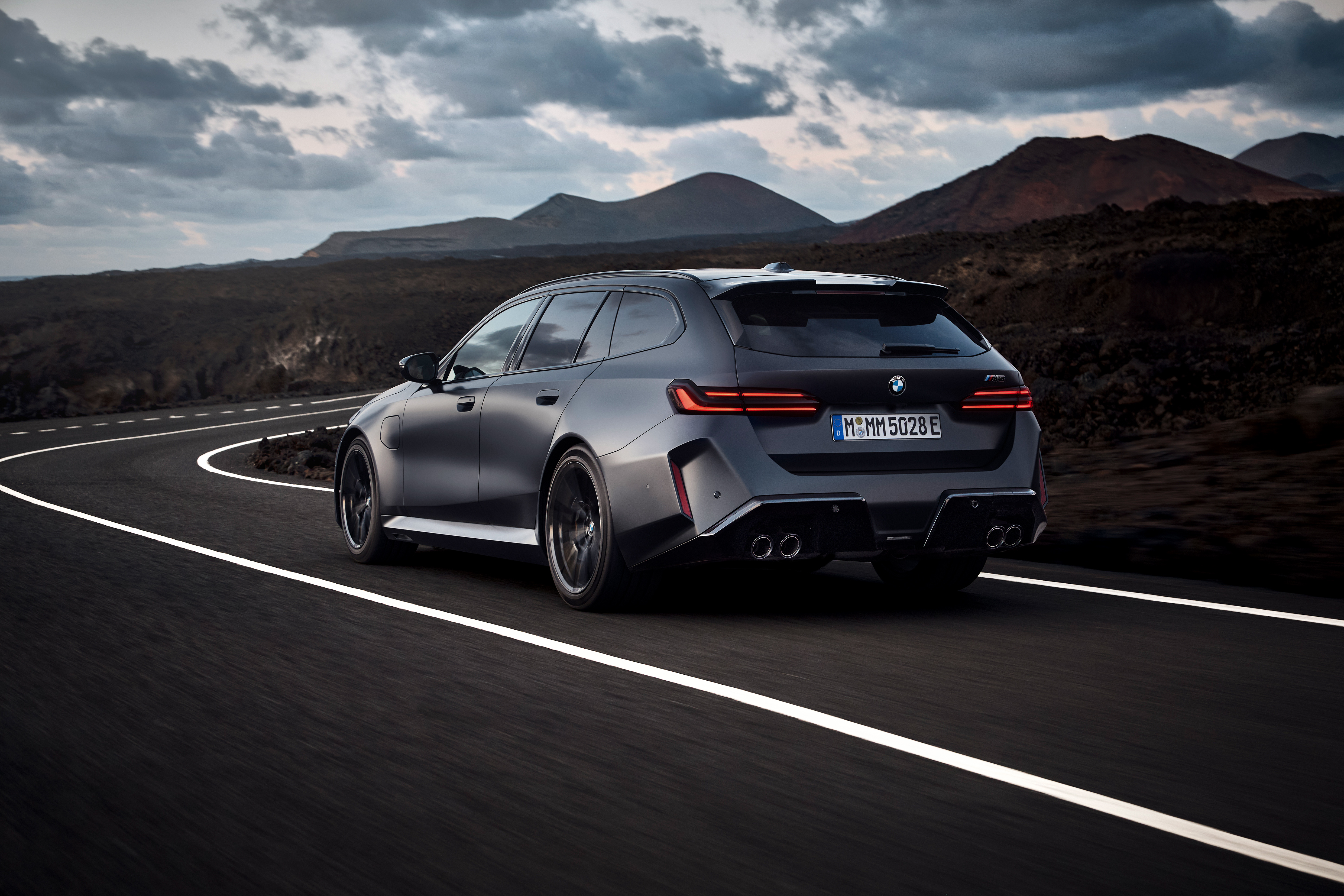 Rear three-quarter view of the BMW M5 Touring cornering on a mountain road.