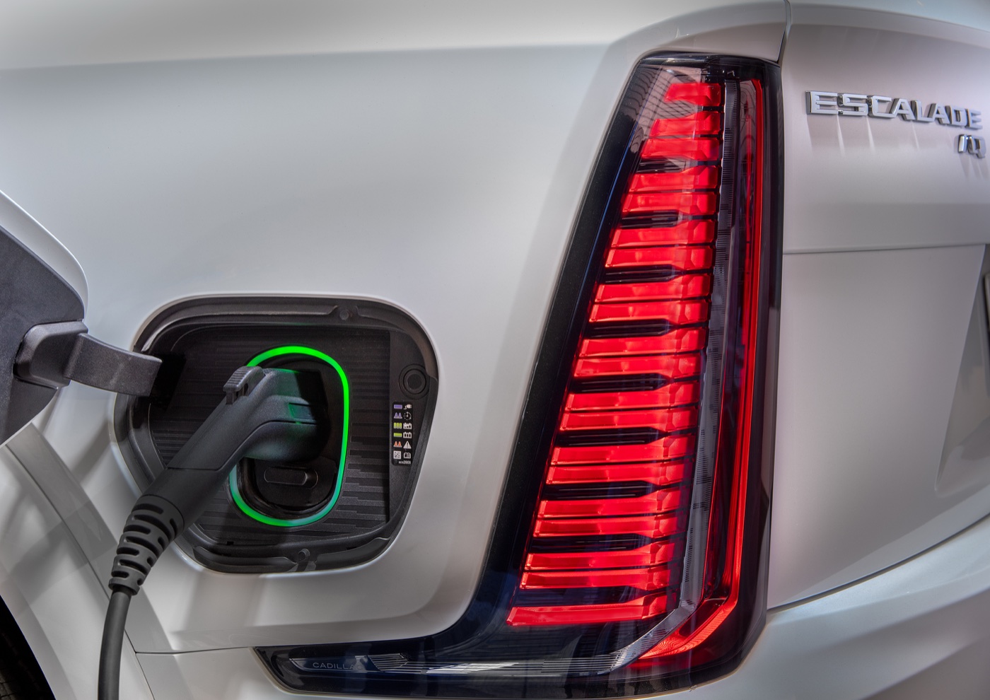 A charging cable plugged into the Escalade IQ charge port beside the vertical rear light bar.