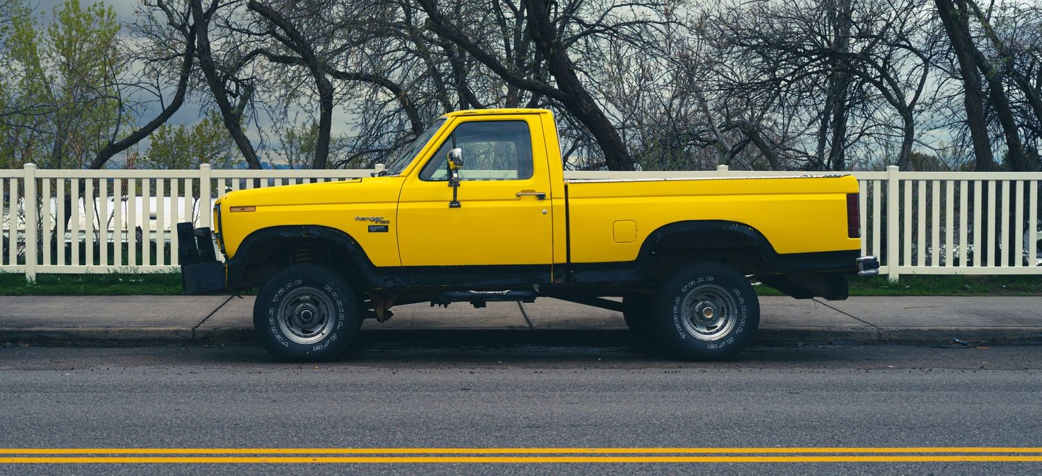 A yellow pickup truck from the side, cab and open cargo bed clearly separate.