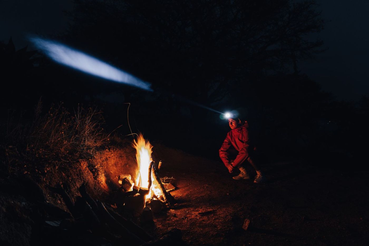 Camper wearing a lit headlamp beside a campfire at night