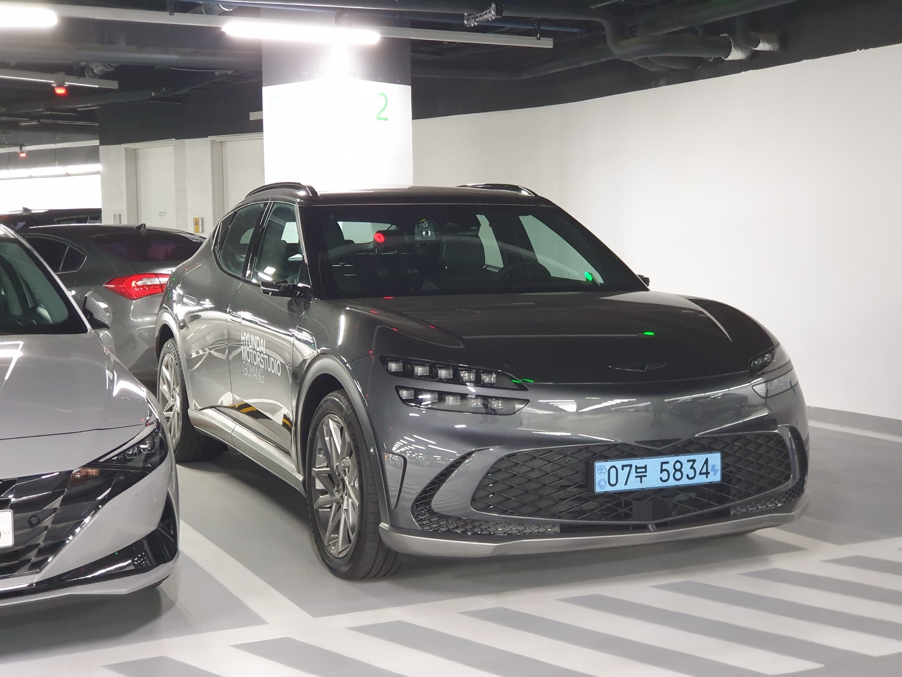 Genesis GV60 in Carbon Metal grey, front three-quarter view, dealership photography.