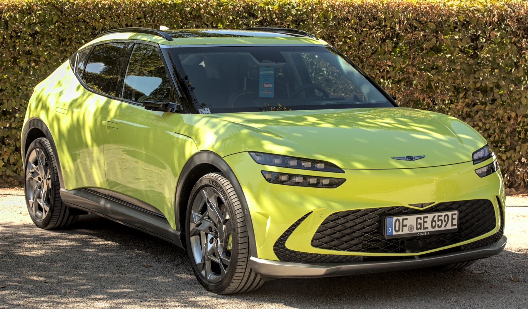 Genesis GV60 in a light green finish, front three-quarter view, parked.