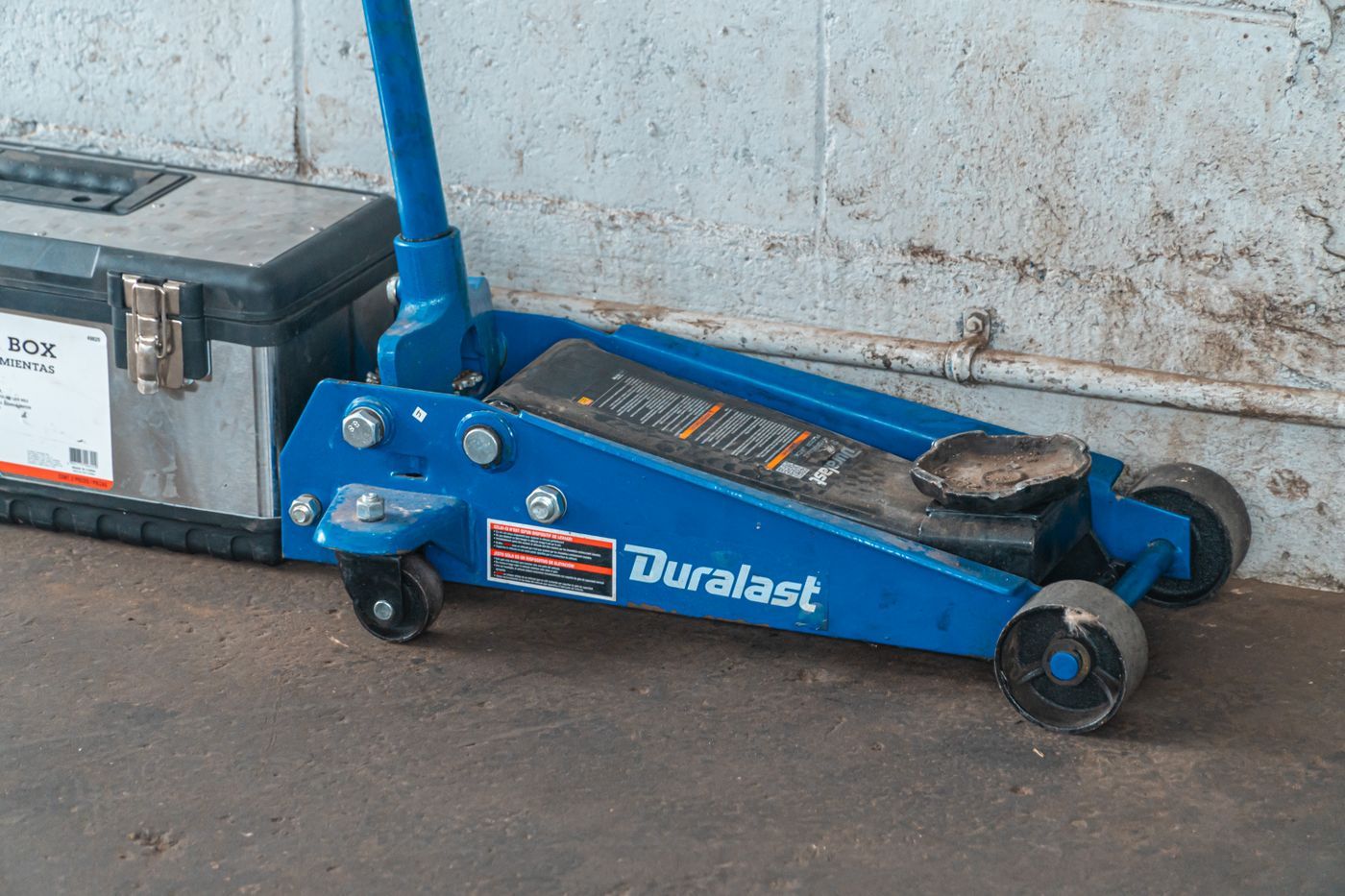 A floor jack and toolbox against a garage wall