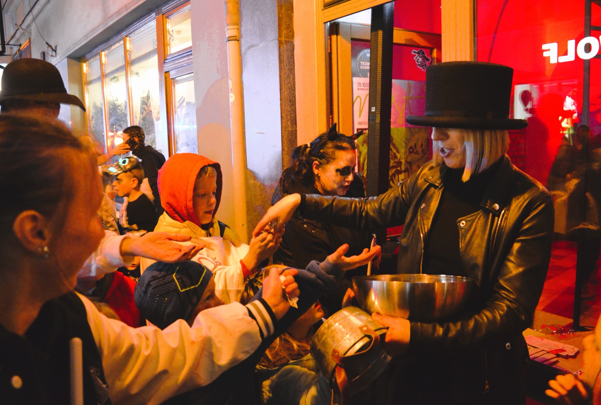 A crowd of trick-or-treaters in costume outside a shop at night, a real photograph.