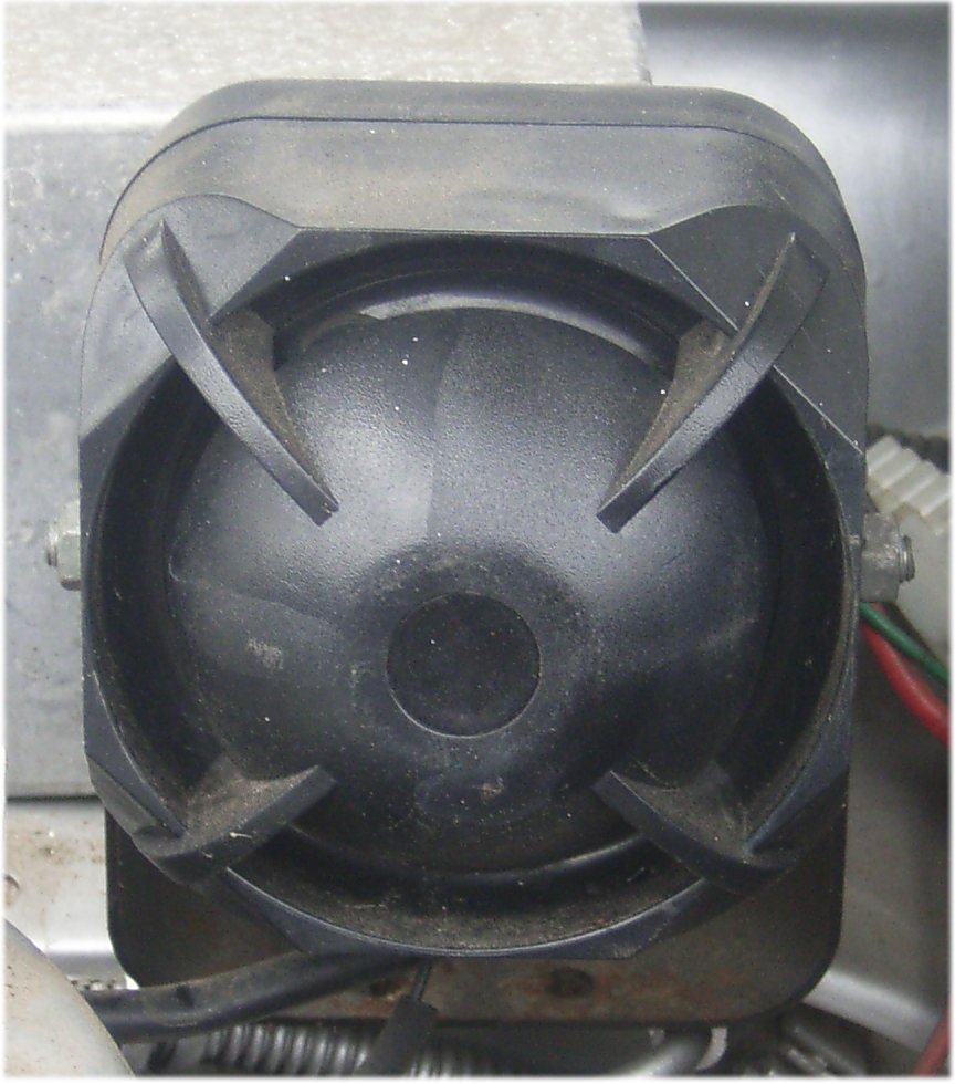 A car alarm siren unit as actually installed in an engine bay, real photograph.