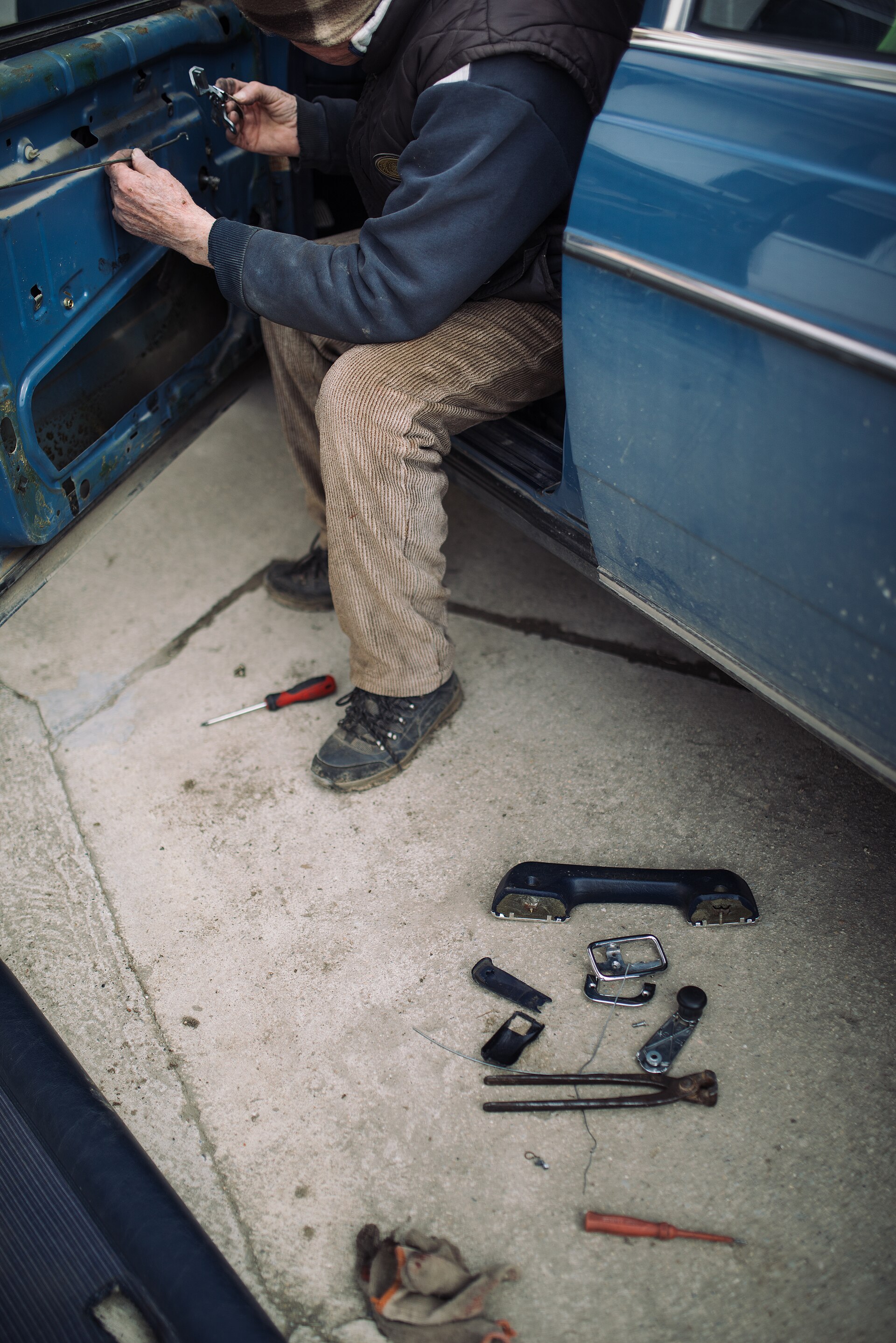 A mechanic working on a car's exterior mechanical door lock, real photograph.