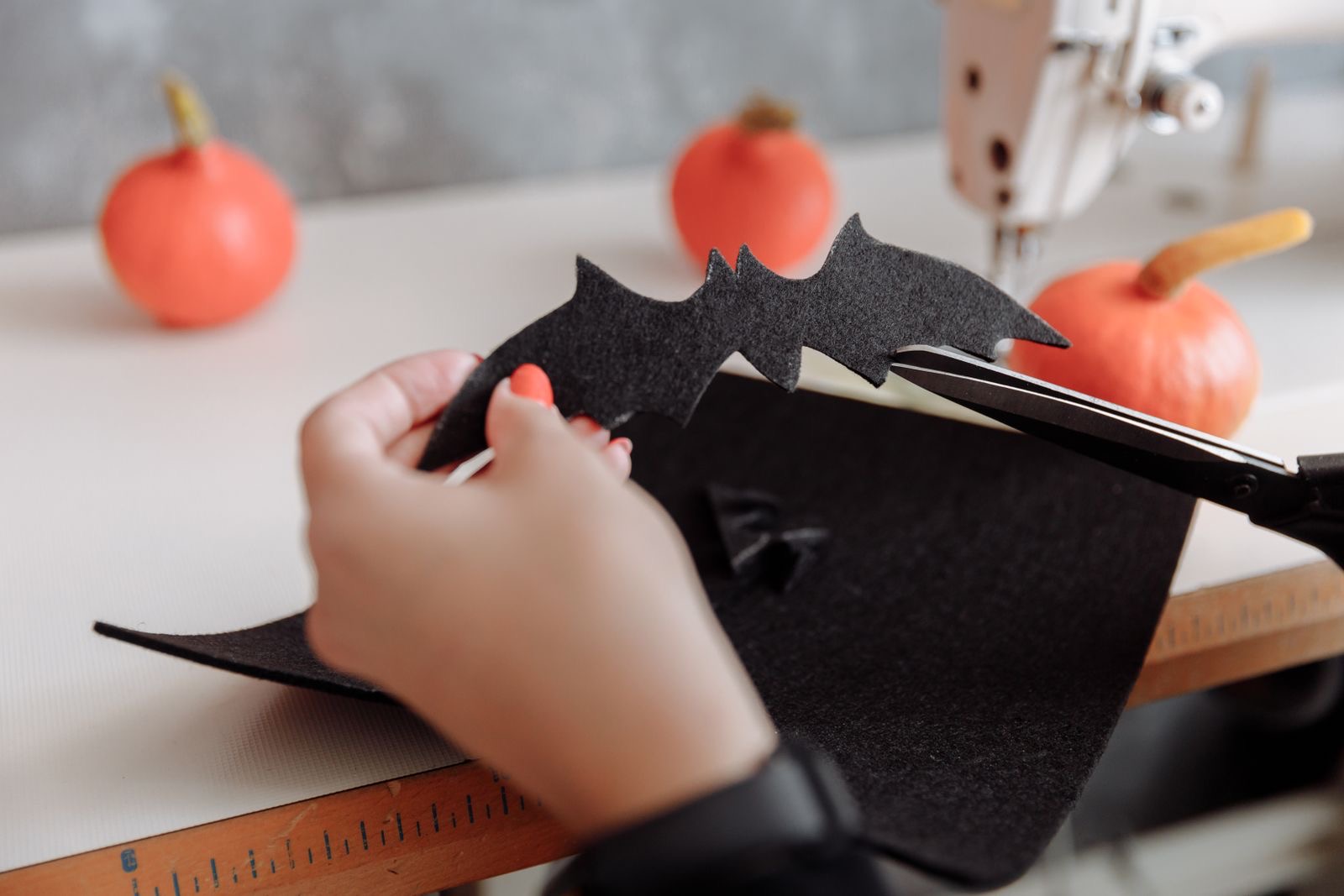 Hands cutting a black felt bat shape with scissors next to small pumpkins.