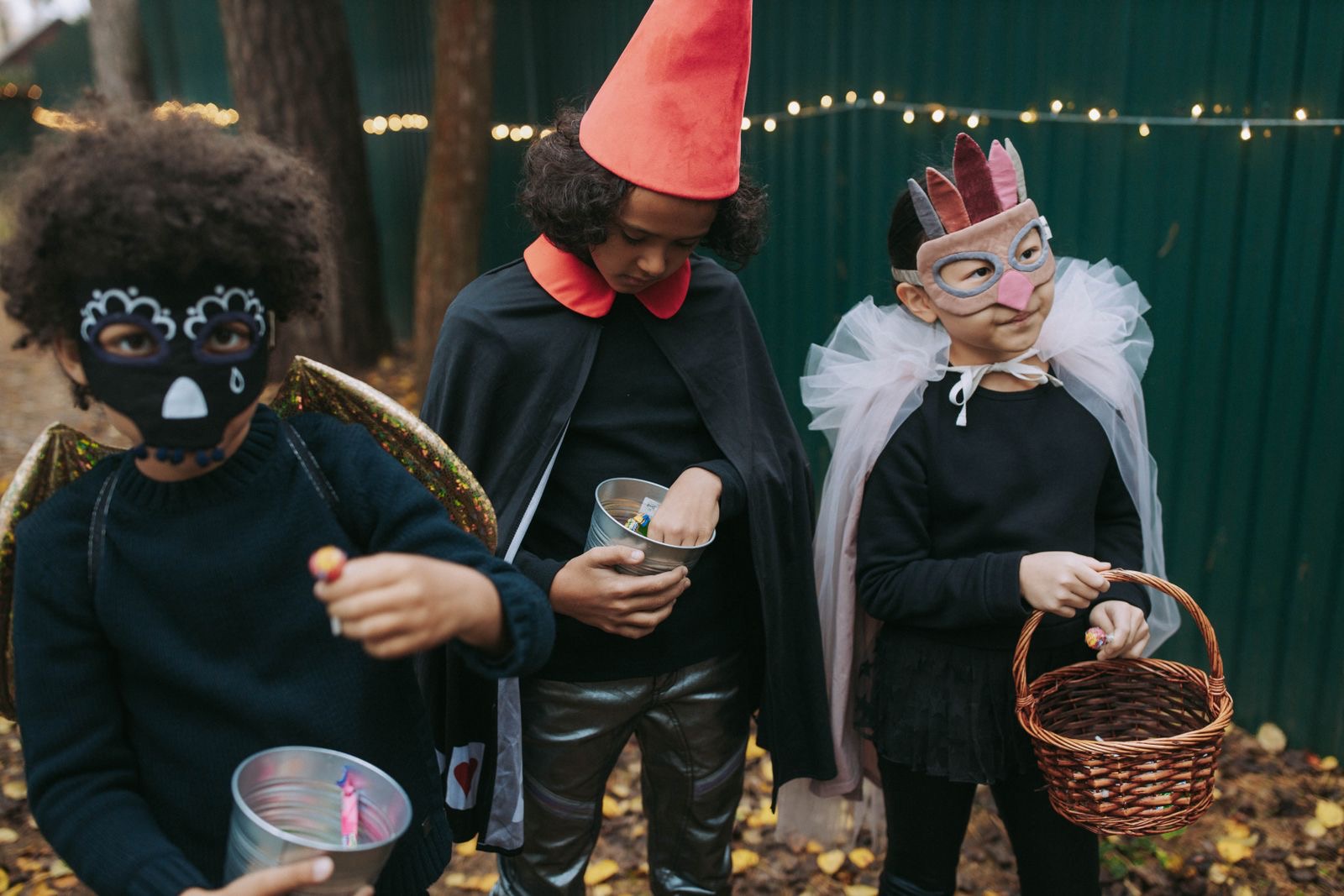 Three children in creative Halloween costumes collecting candy outdoors.