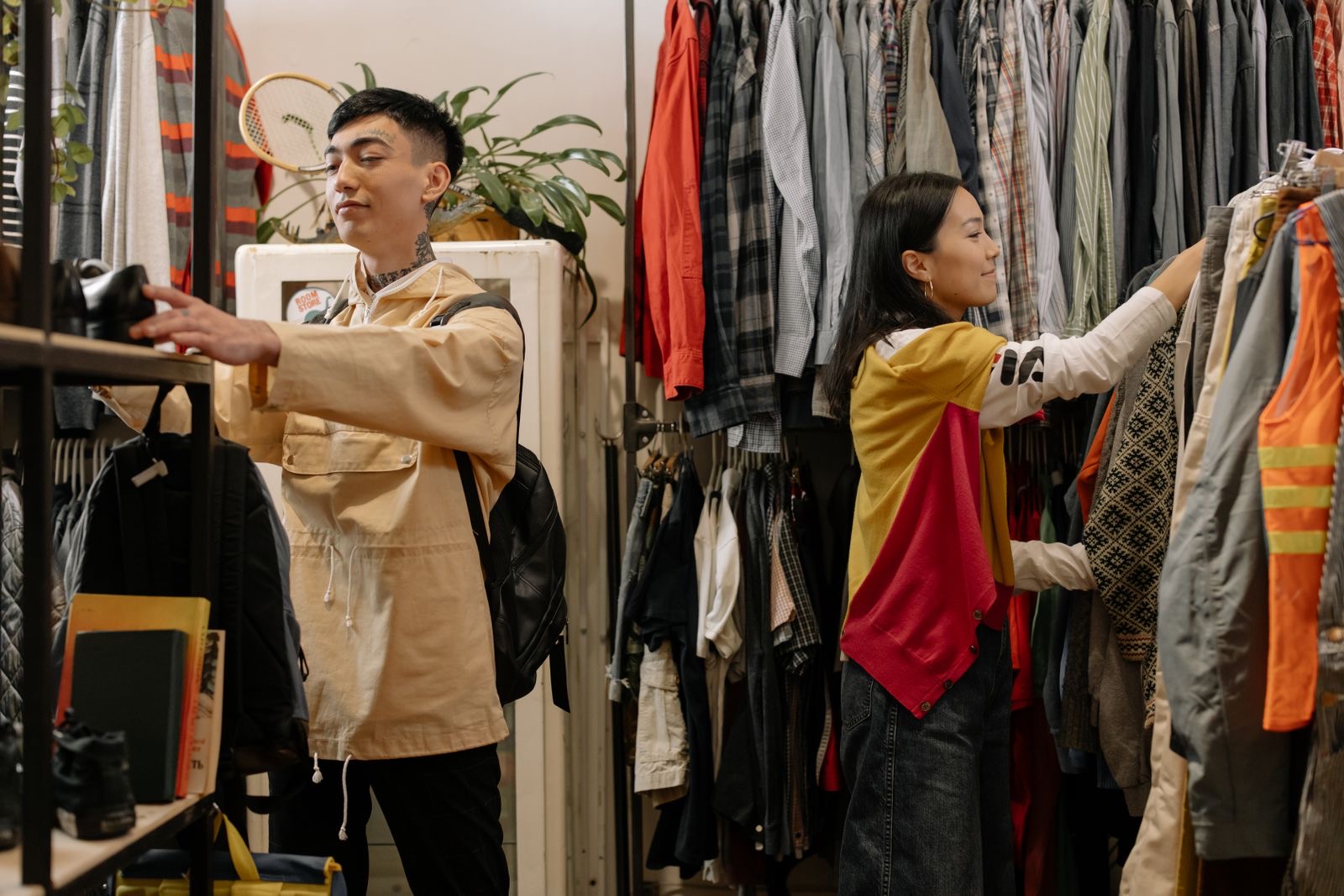 Two young adults browsing clothes in a crowded vintage thrift store.