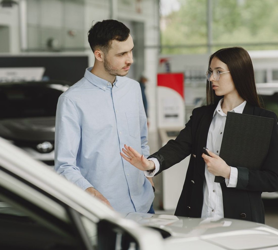 A buyer and a salesperson talking across a car on a dealership showroom floor