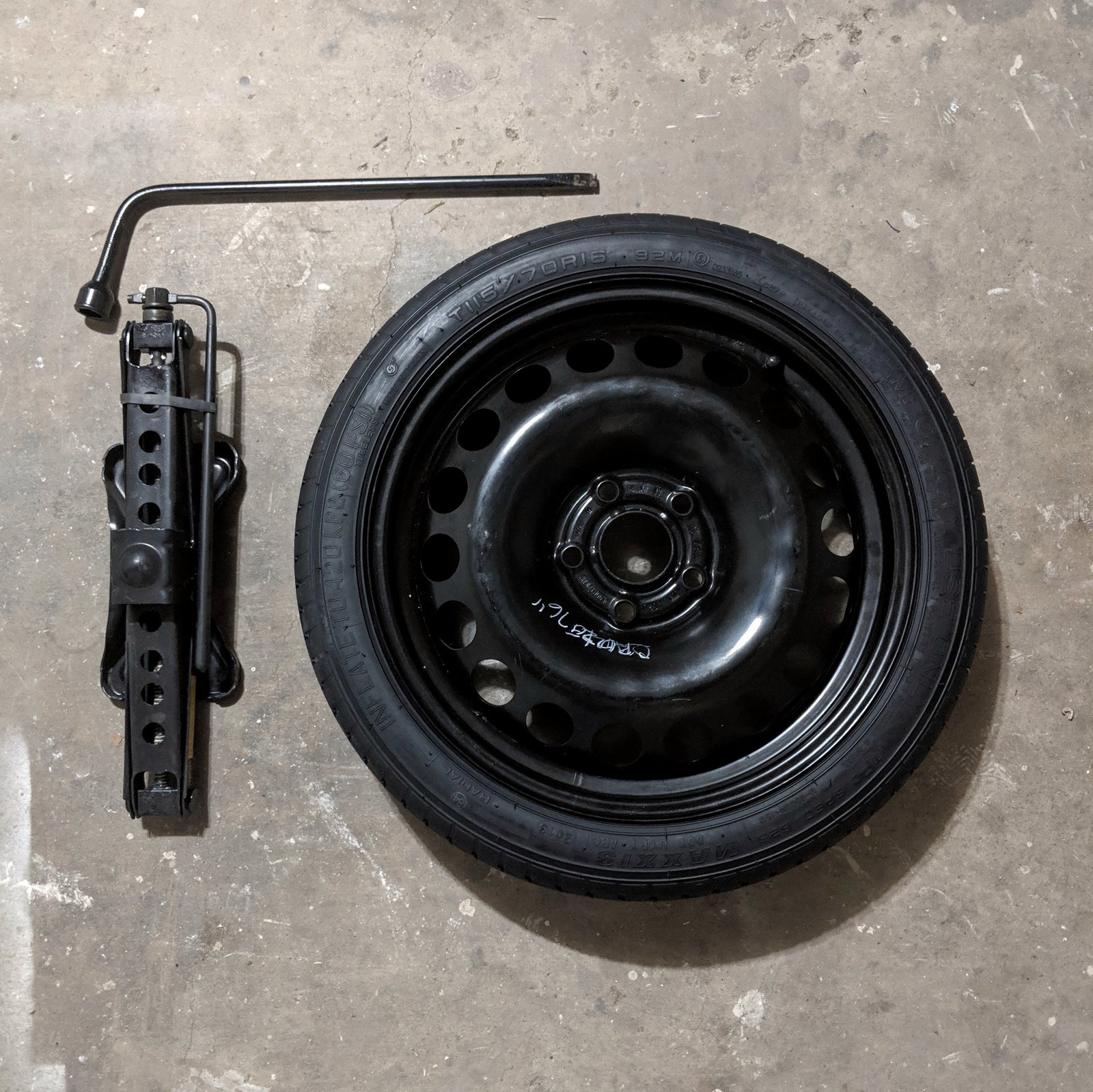 A spare tire, scissor jack, and lug wrench laid out — the tools kit needed for a tire change
