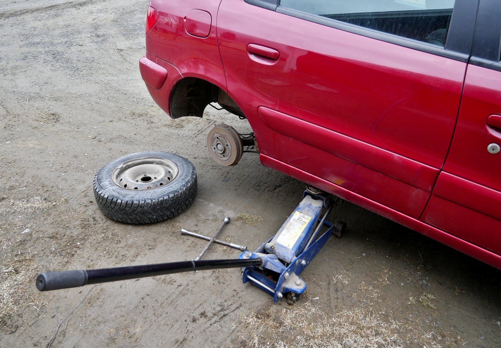 A floor jack correctly positioned under the vehicle's reinforced body sill, not the bumper or the tire