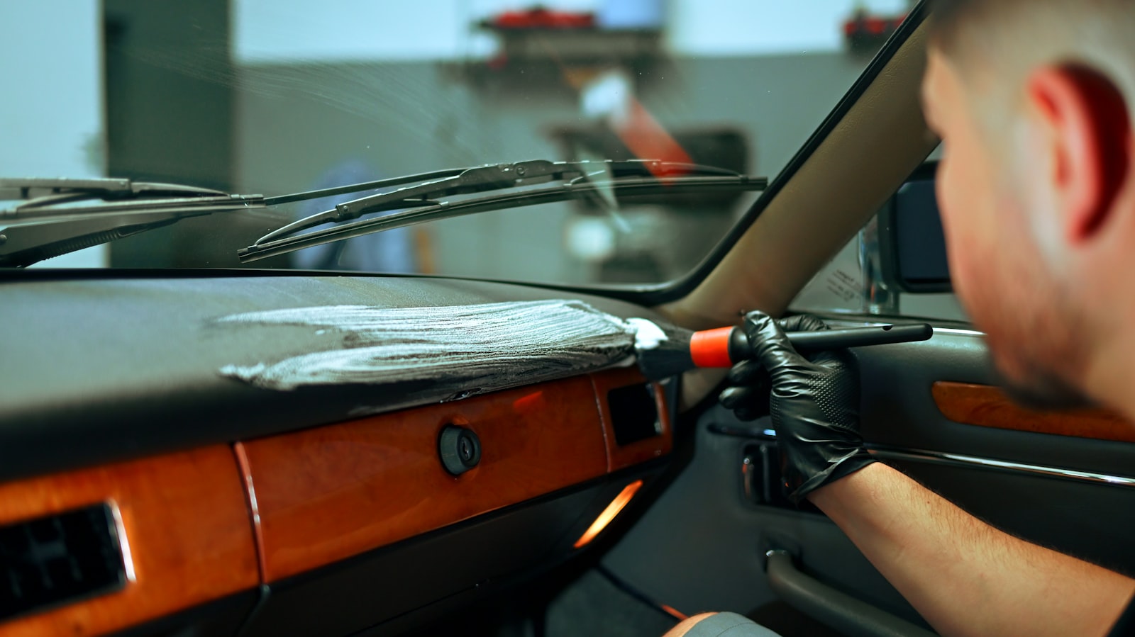 A person cleaning a car dashboard interior with a brush.