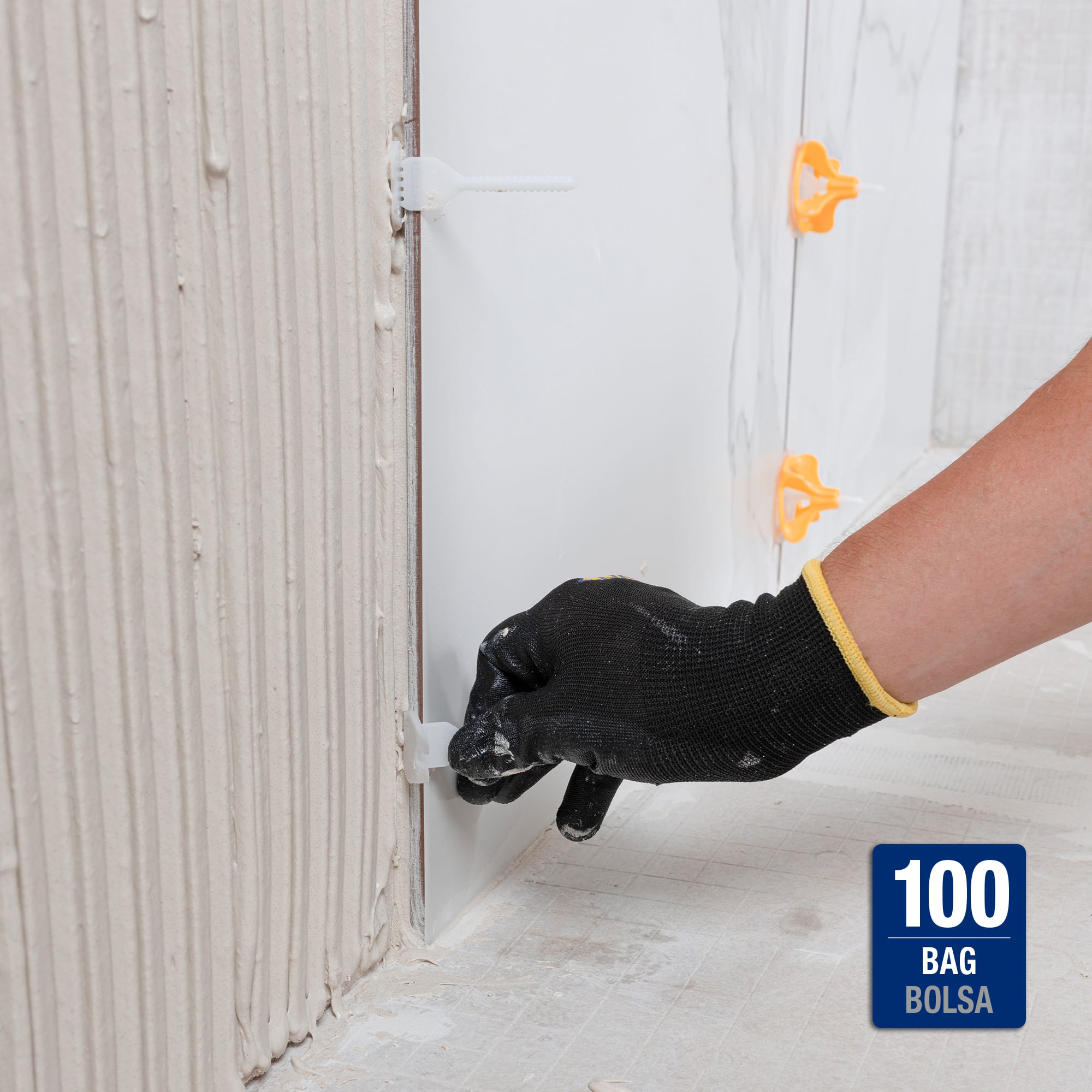 A gloved hand installing a plastic leveling clip between two large-format wall tiles during installation, with additional clips visible along the grout lines.