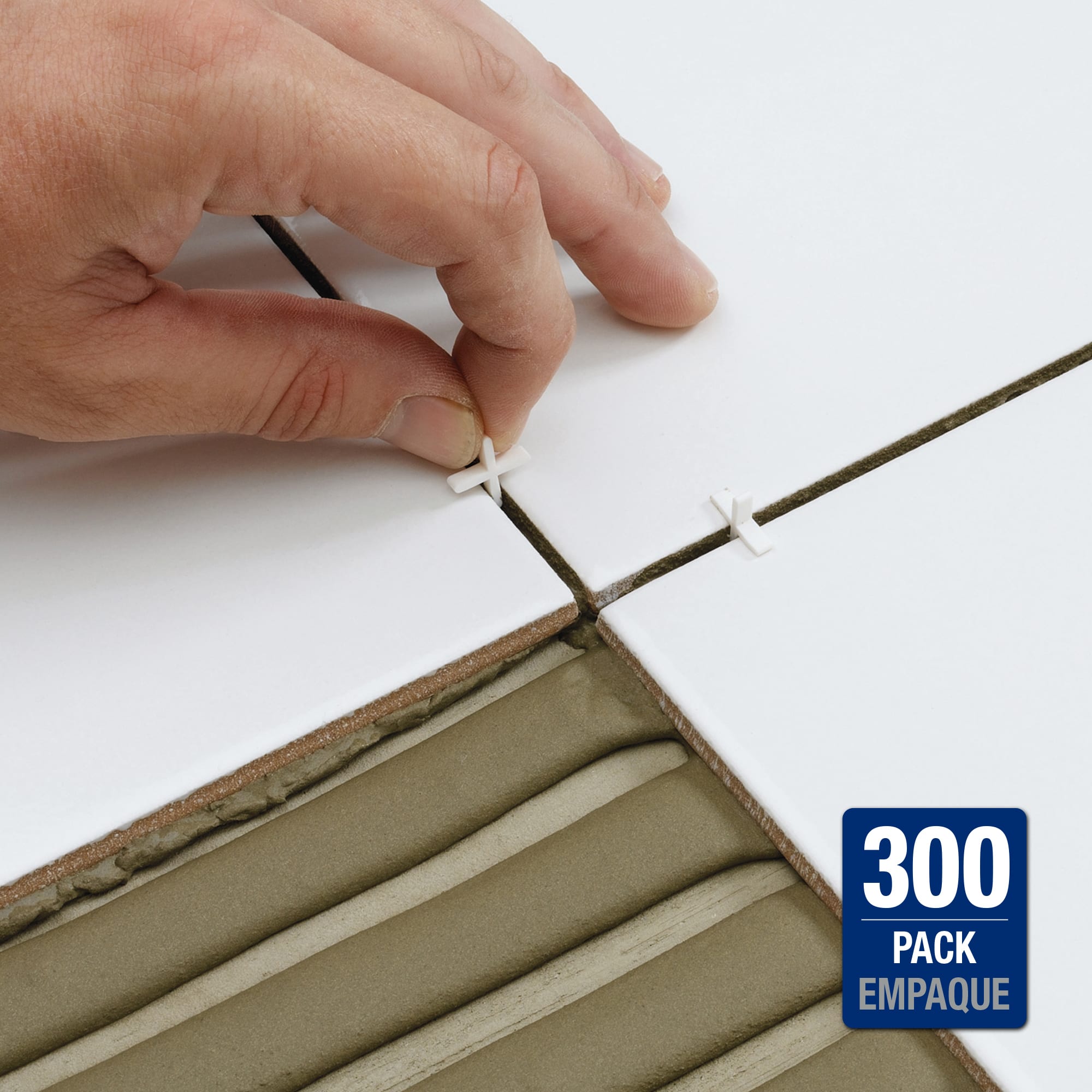 A hand placing a plastic cross-shaped tile spacer into the joint between two freshly set wall tiles, with wet thinset visible on unset tiles behind.